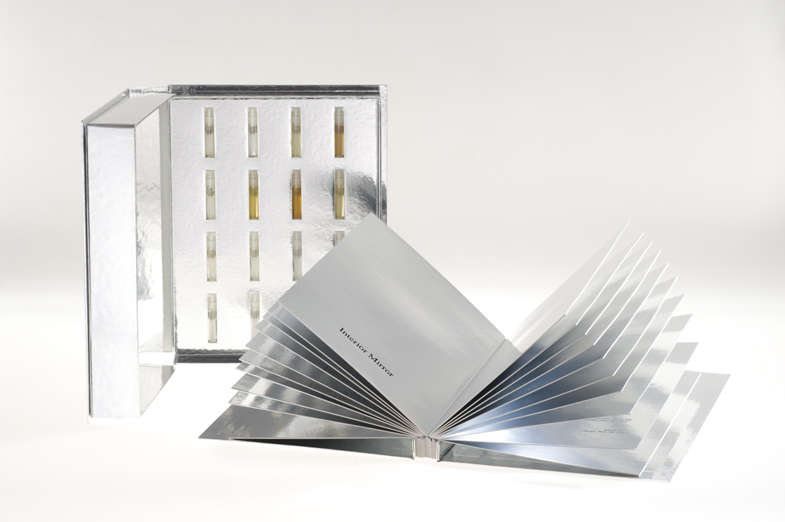 a silver book with a cover behind that contains many small vials of fragrance