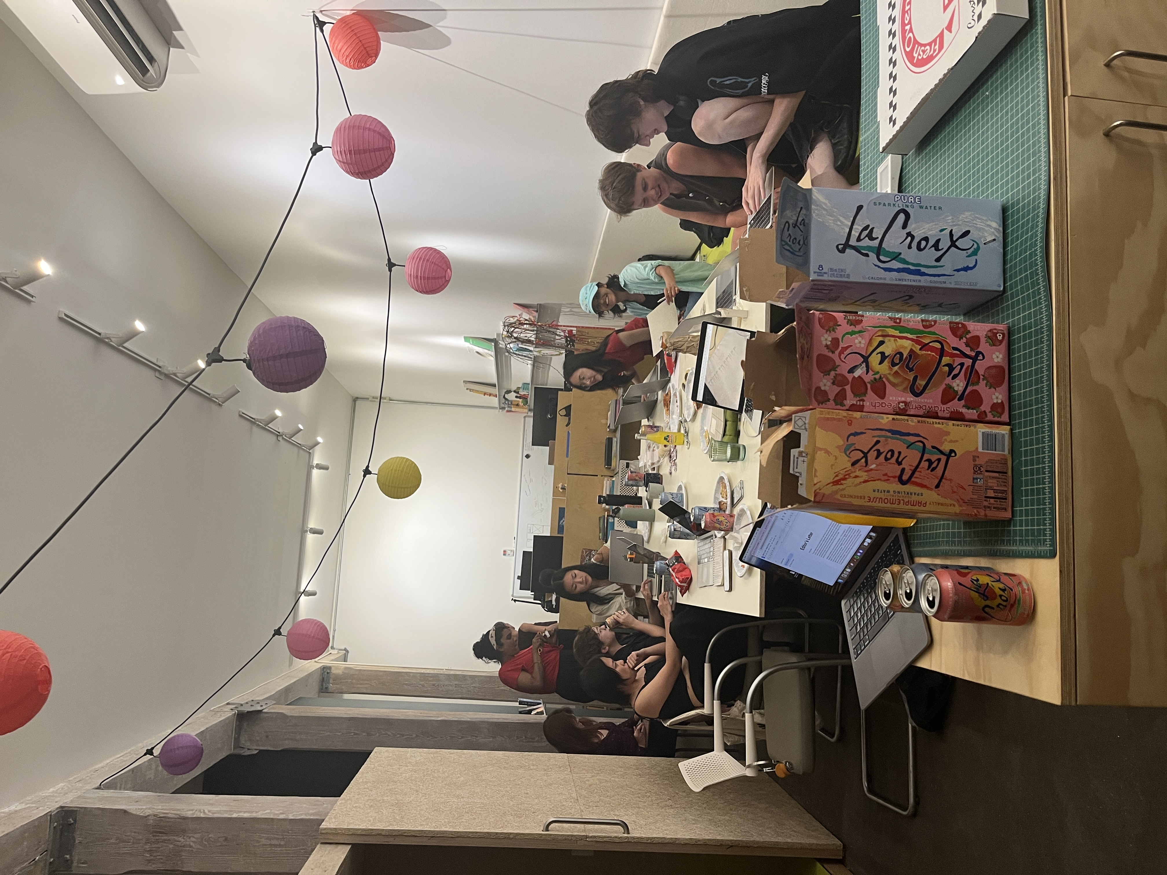 groups
cluster around the table to discuss the publication on the last day
of class, with La Croix and pizza visible in the foreground