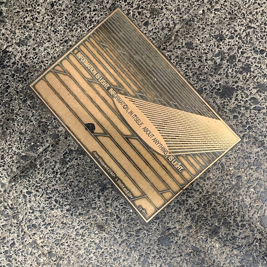 a plaque on the sidewalk that says 'Information is light. Information, in itself, about anything, is light.' - Tom Stoppard (1937- ) with beams of light falling to the floor