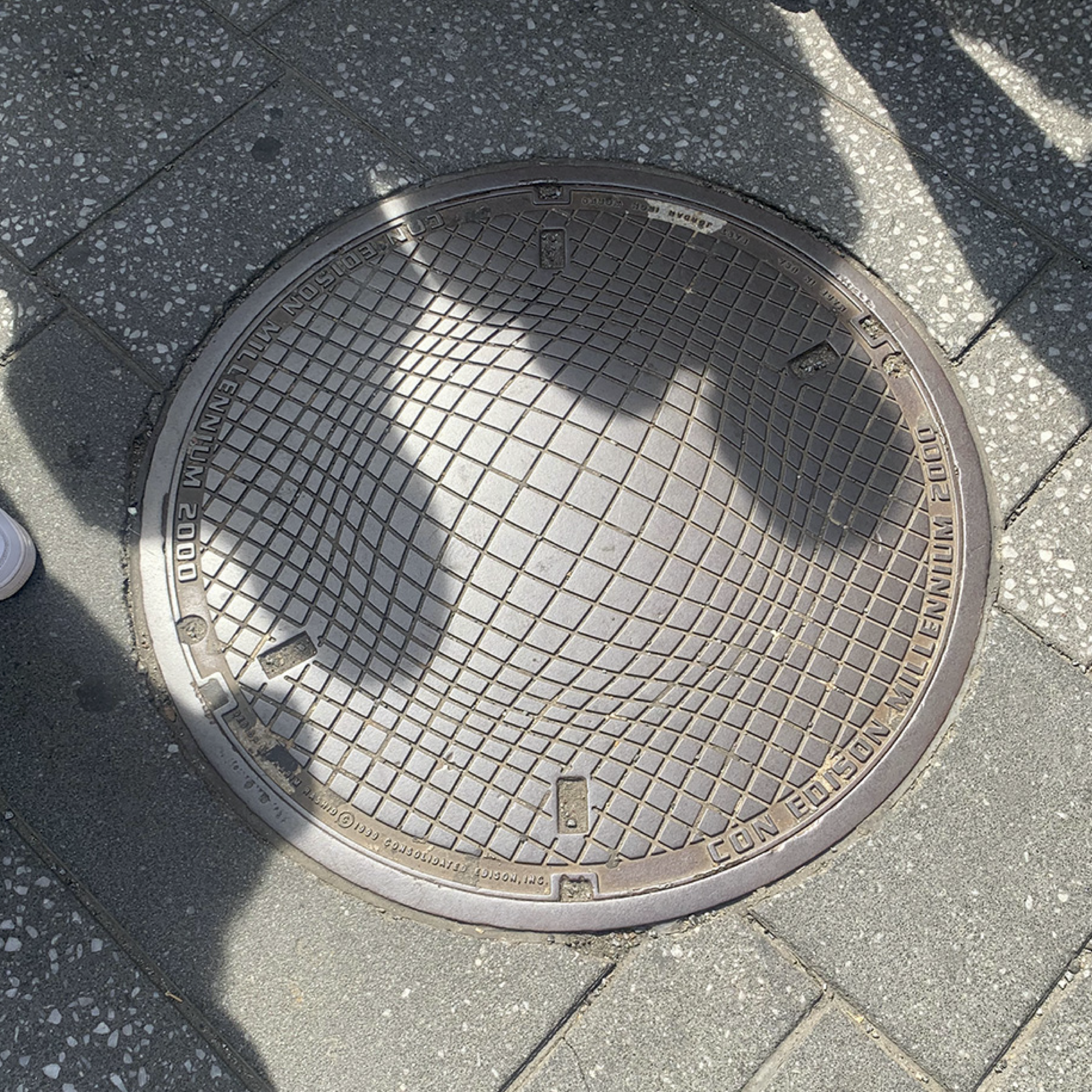 Manhole cover with a breaking-the-matrix design of a spherical object coming into a grid, like when Flatland is entered by a sphere